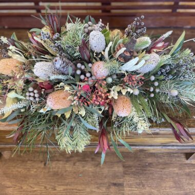 Elegant wildflower casket spray featuring a mix of Australian native blooms such as Protea, Banksia, and Eucalyptus, arranged in a respectful and serene design for a dignified tribute