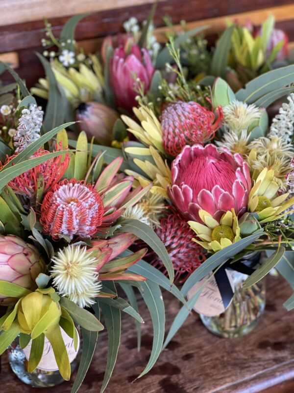 Charming wildflower posy jar showcasing native Australian flowers such as banksia,leucadendrons,soft gum leaves arranged in a simple glass jar for a fresh, natural look